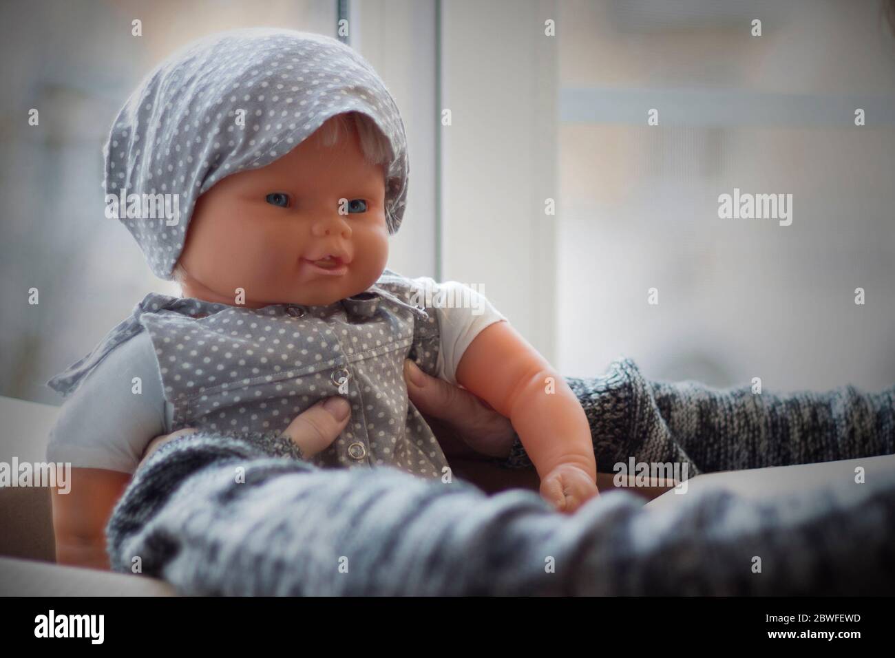 Die Hände des Mädchens nehmen die Puppe aus der Kiste. Puppe in einem grauen Sonnenkleid und Schal auf einem hellen Hintergrund. Stockfoto
