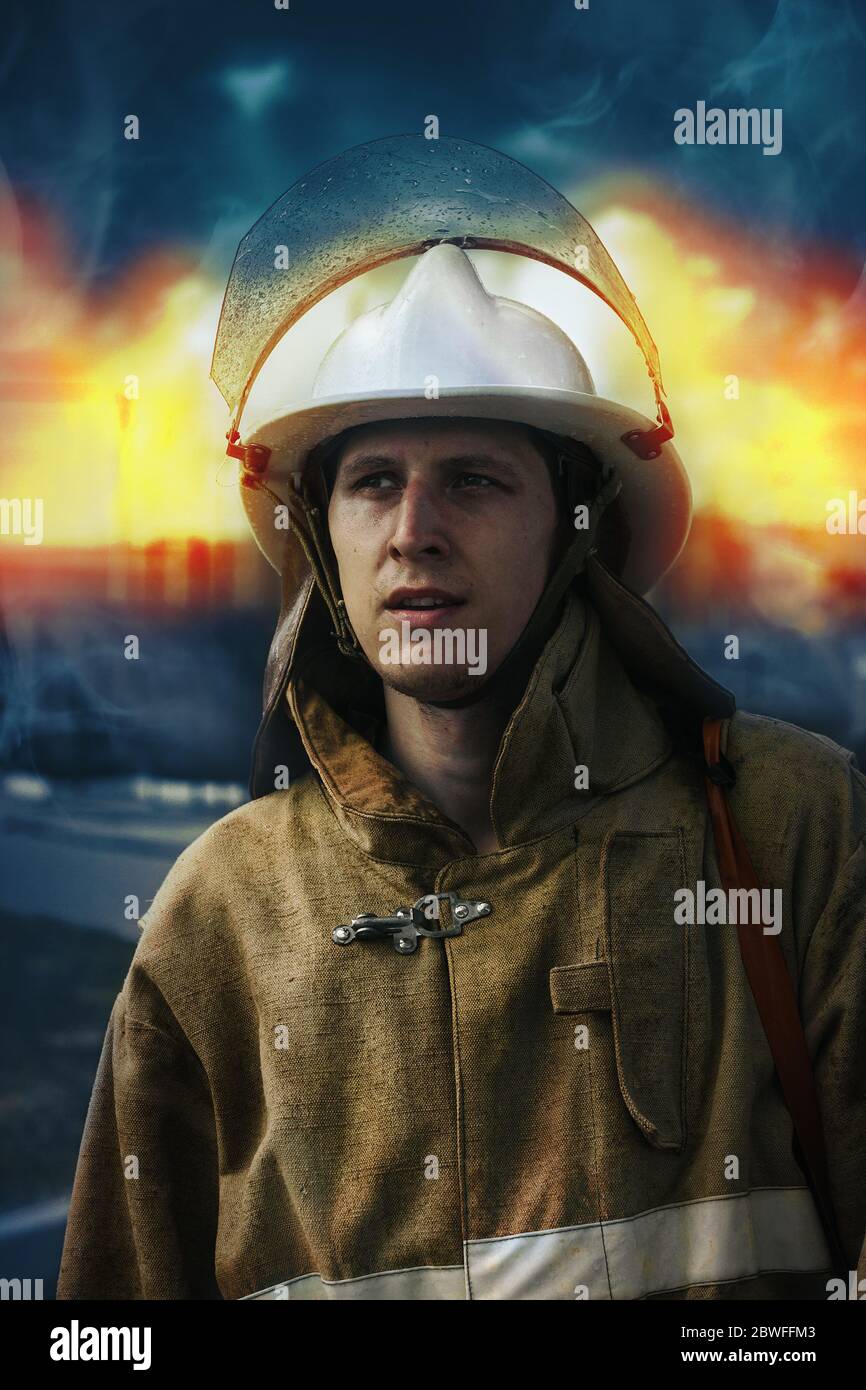 Porträt eines Feuerwehrmundes in Helm und Spezialkleidung vor dem Hintergrund des Feuers. Ein junger Retter der kaukasischen Nationalität Stockfoto