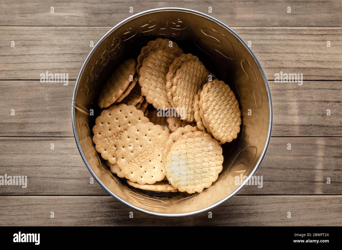 Nahaufnahme und Draufsicht von integralen Keksen auf einer runden Metallbox auf einem Holztisch. Stockfoto