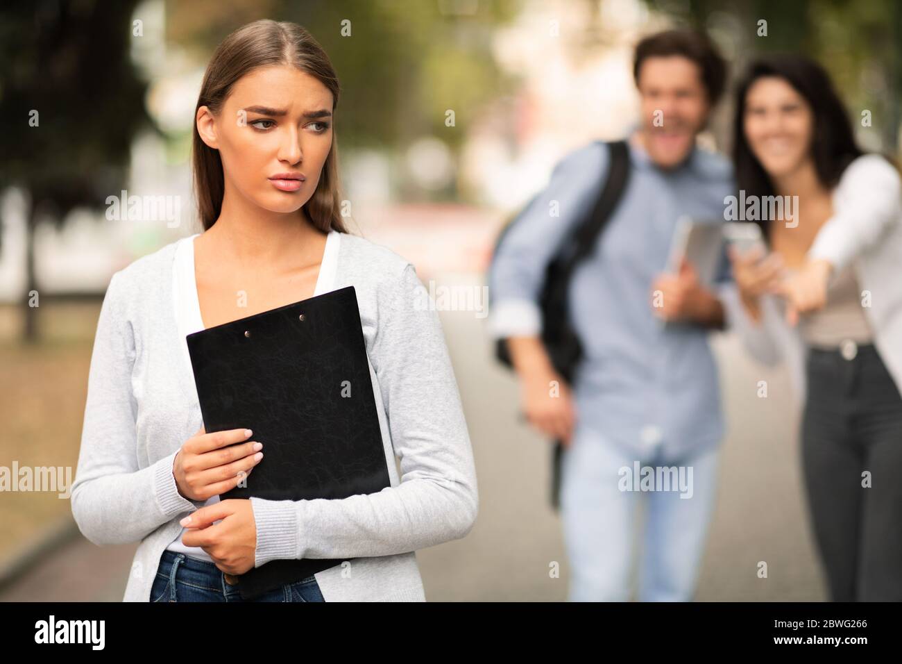 Unglückliches Mädchen, Das Von Ein Paar Studenten Gemobbt Wird, Die Draußen Spazieren Gehen Stockfoto