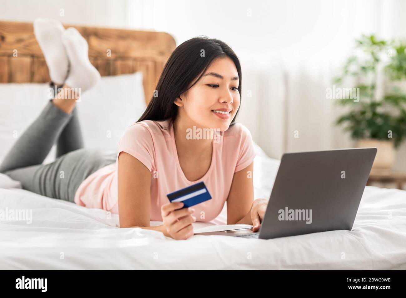 Asiatische Frau Online-Shopping Mit Laptop Liegend Auf Bett Indoor Stockfoto