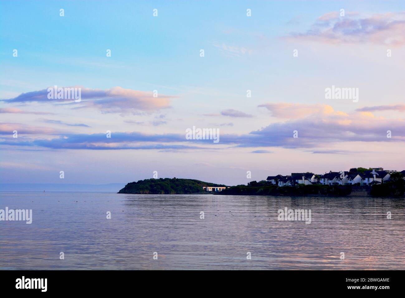 Barry, Wales, der Damm und Punkt auf Barry Island am Horizont. Flut mit Sonnenuntergang und Wolken über dem Himmel verstreut. Stockfoto
