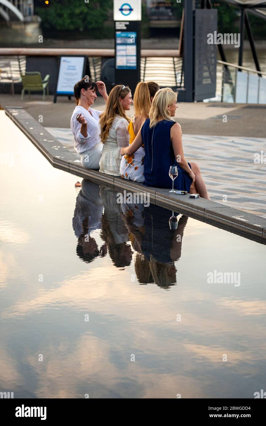 Eine Gruppe von Freundinnen sitzt neben einem Wasserspiel im öffentlichen Raum am Riverside Walk neben dem Battersea Power Station RedeDevelopment, River Thames Stockfoto