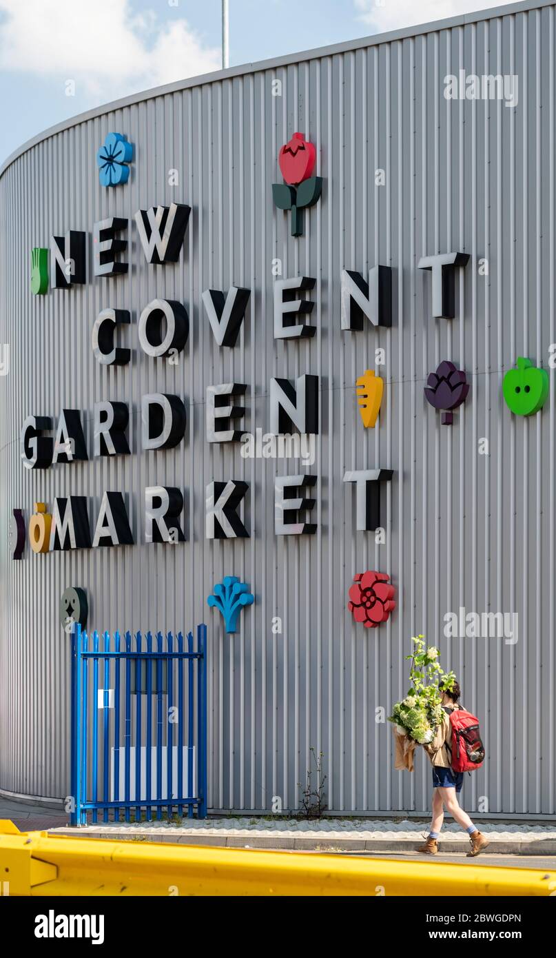 Ein Kunde verlässt den berühmten New Covent Garden Market mit einem Blumenstrauß. Die lesbare Beschilderung ist hinter ihm auf dem Lagerhaus Stil Gebäude Stockfoto