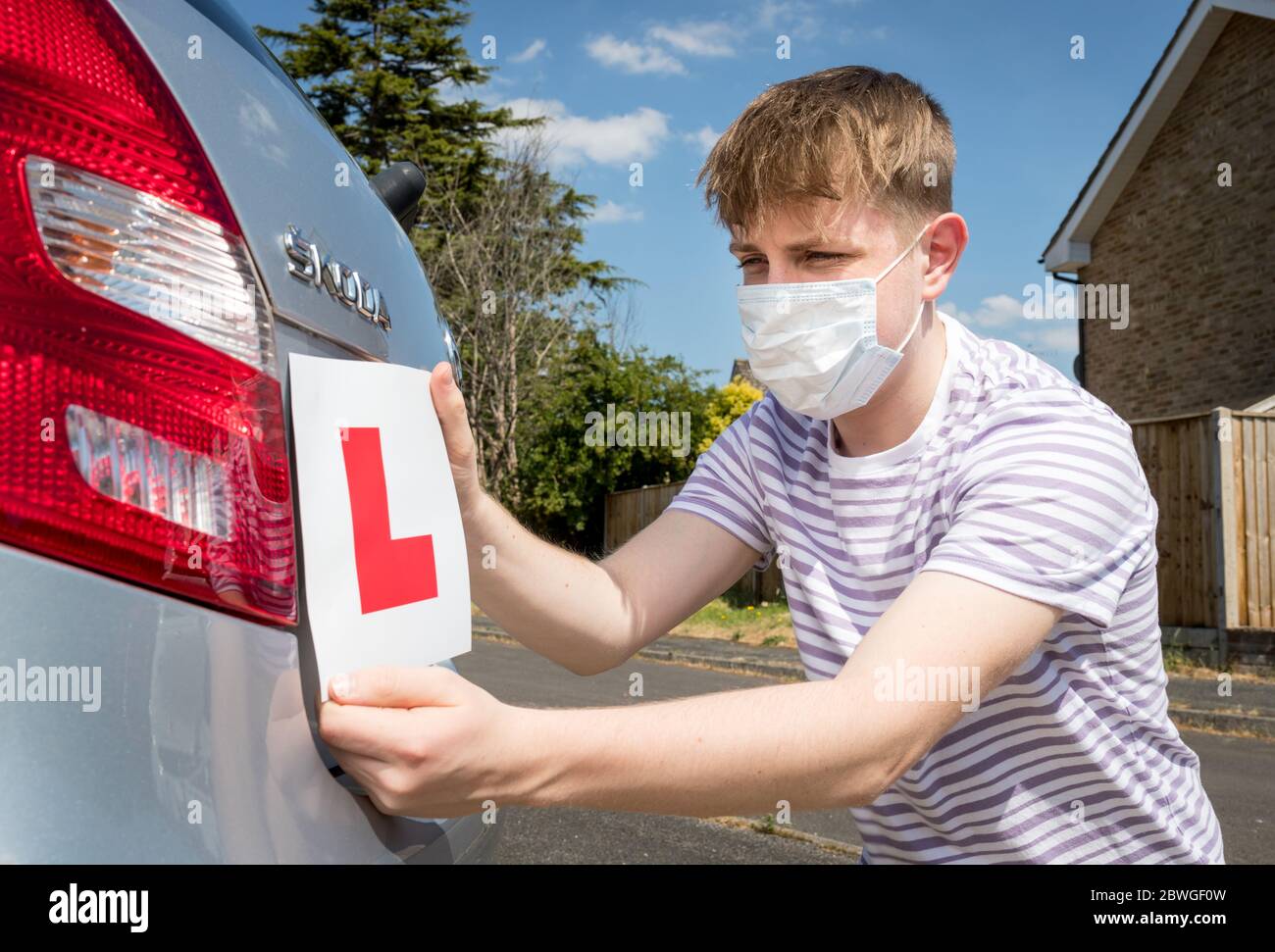 Teenager-Lernfahrer A trägt eine Gesichtsmaske wegen der Coronavirus-Pandemie warten, um seine Fahrstunde zu beginnen. Stockfoto
