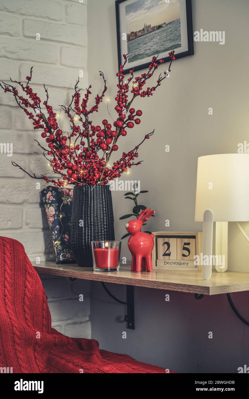 Weihnachtliche Einrichtung zu Hause. Roter Spielelch, Kerze und Vase mit dekorativen Zweigen auf Regal Nahaufnahme Stockfoto