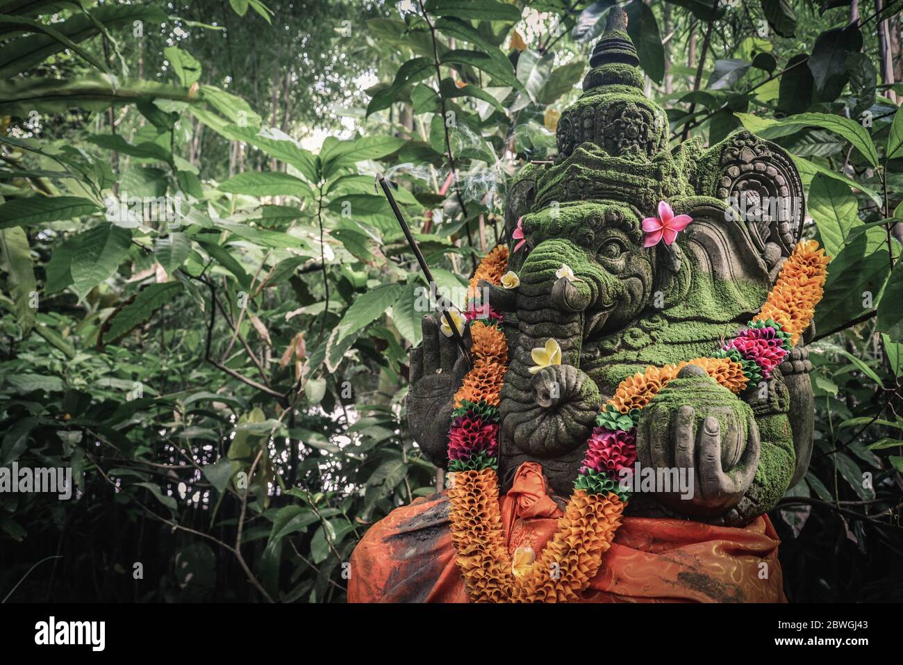 Stein Ganesha Statue mit den Räucherstäbchen und orange Blumen für religiöse Fest und zeremonielle Darbringung, Bali dekoriert. Stockfoto