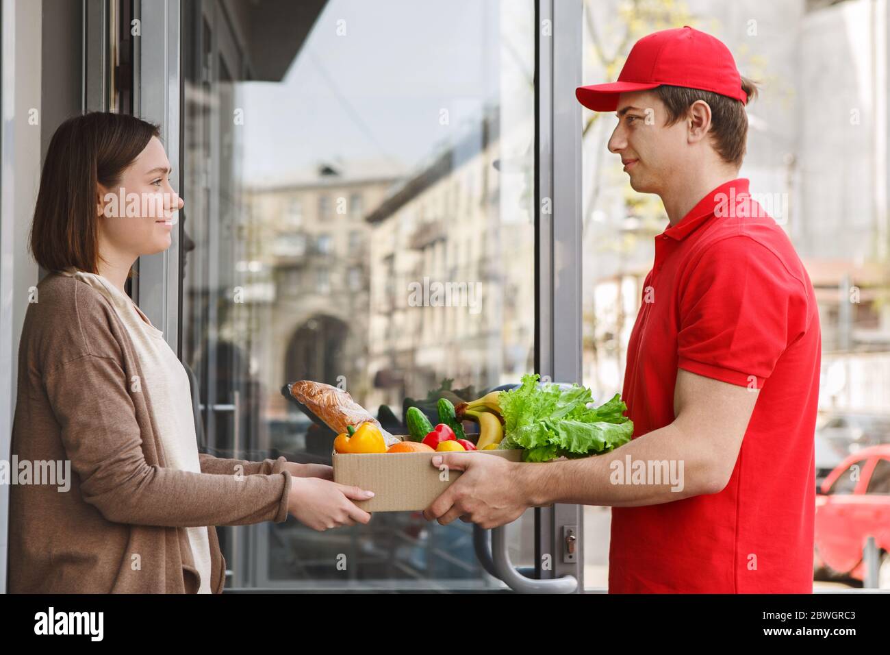 Lieferung von Produkten zu Hause. Kurier gibt Box mit Essen an Mädchen Stockfoto