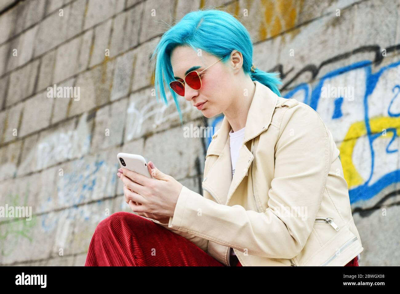 Kiew, Ukraine - 22. April 2019: Schöne junge kaukasische Mädchen mit blauen Haaren verwendet iPhone XS im Freien Stockfoto