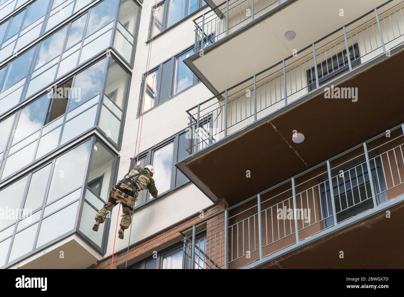 Außerhalb des mehrstöckigen Gebäudes Waschen der Fassade eines Industriekletterers saubere Fenster, Ansicht von unten. Arbeiter Alpinist Stockfoto