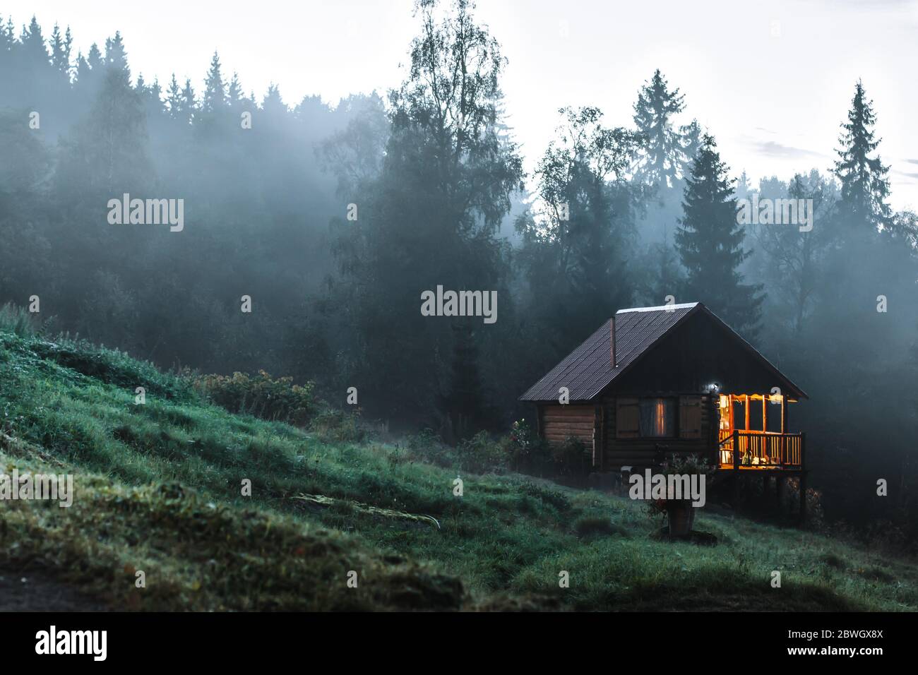 Kleines altes Holzhaus in nebligen Wald. Berglandschaft. Konzeptionelles Naturbild Stockfoto