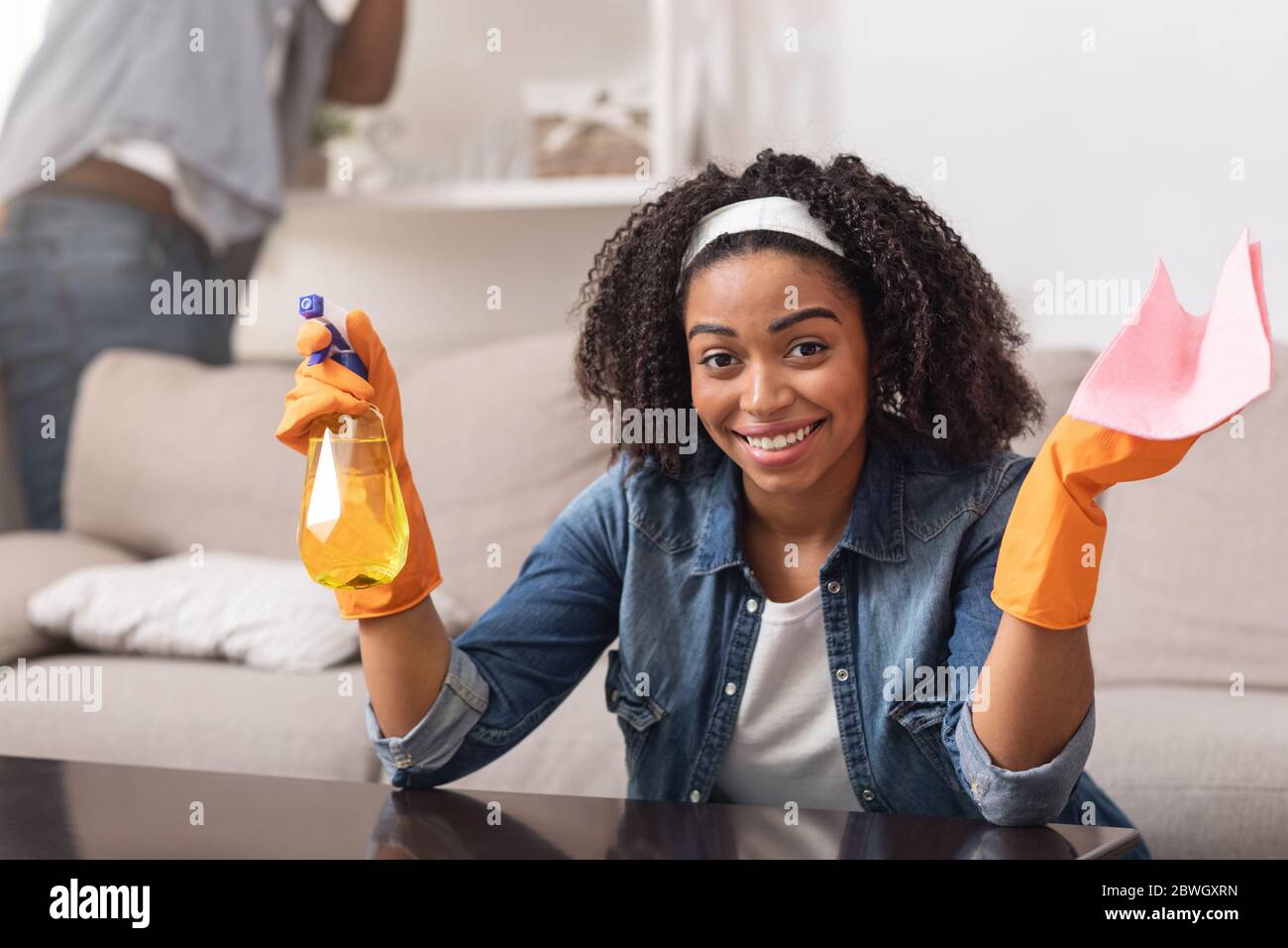 Lächelnde Schwarze Hausfrau, Die Rag Und Sprayer Hält, Reinigungstisch Zu Hause Stockfoto
