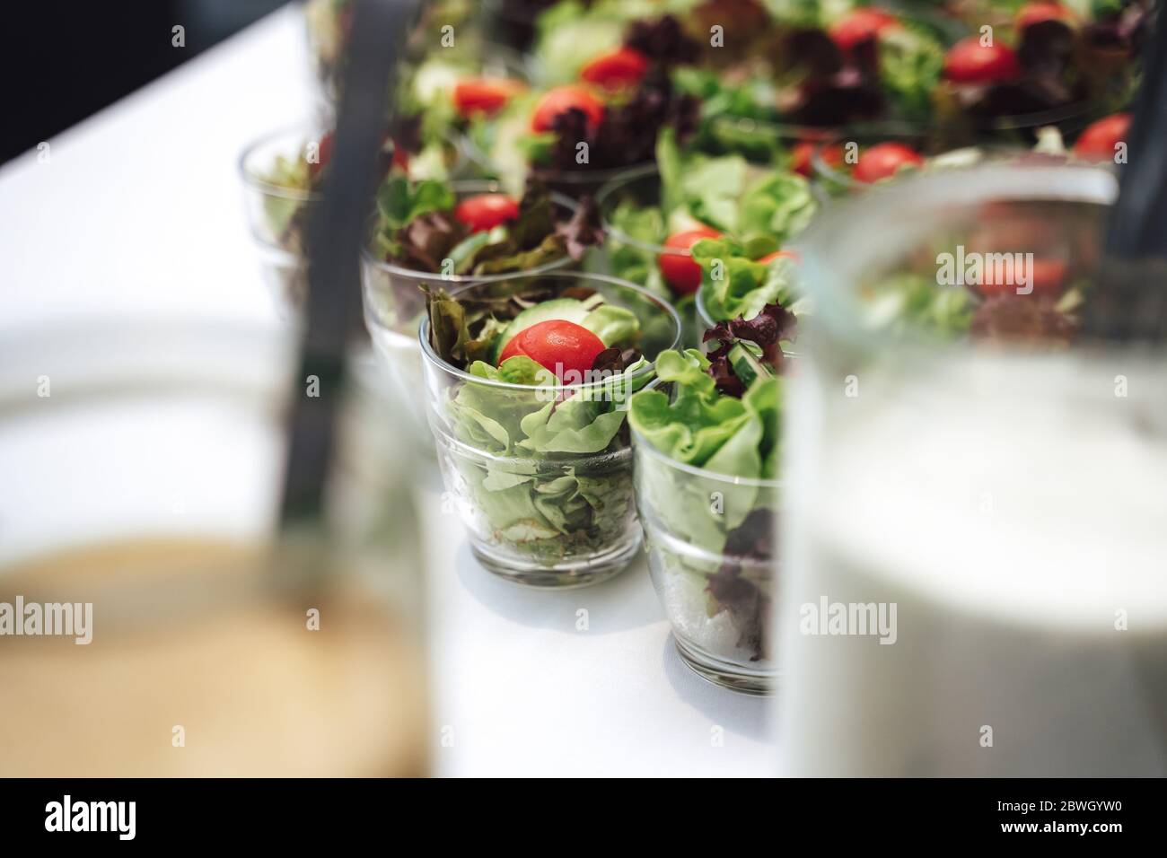 Gläser mit Gemüsesalat in Reihe. Salat, Tomaten und Gurken in Scheiben geschnitten. Feier, Party, Geburtstag oder Hochzeit Konzept. Stockfoto