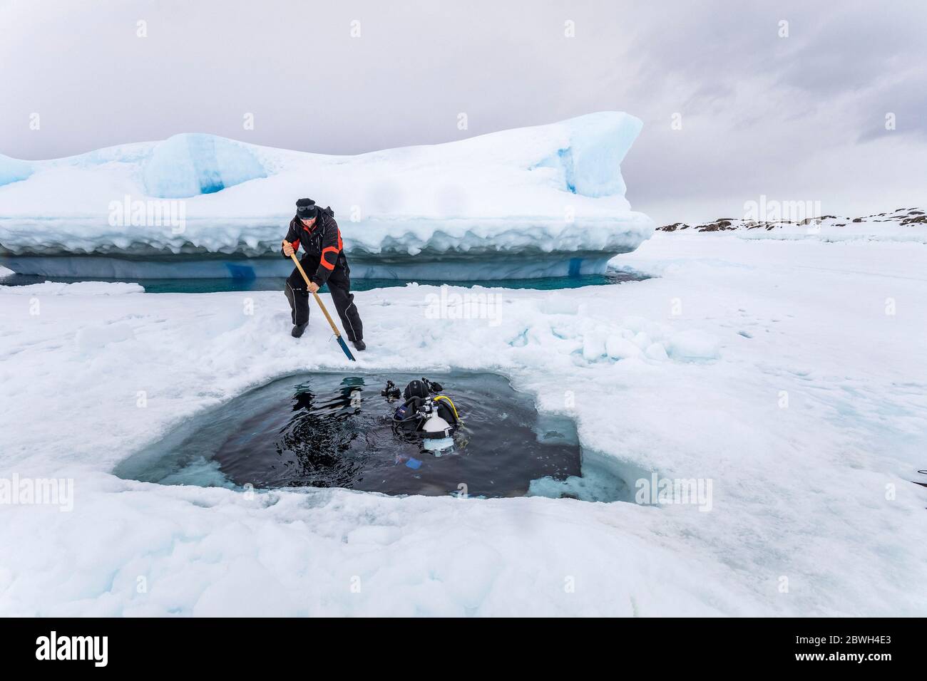 Die Säge verwenden, um das Eis zu schneiden und den Eintritt zu machen, um unter dem Eis zu tauchen. Auf der Rückseite taucht die Spitze des Eisbergs aus der gefrorenen Meeresoberfläche auf, sie bewegt sich Stockfoto