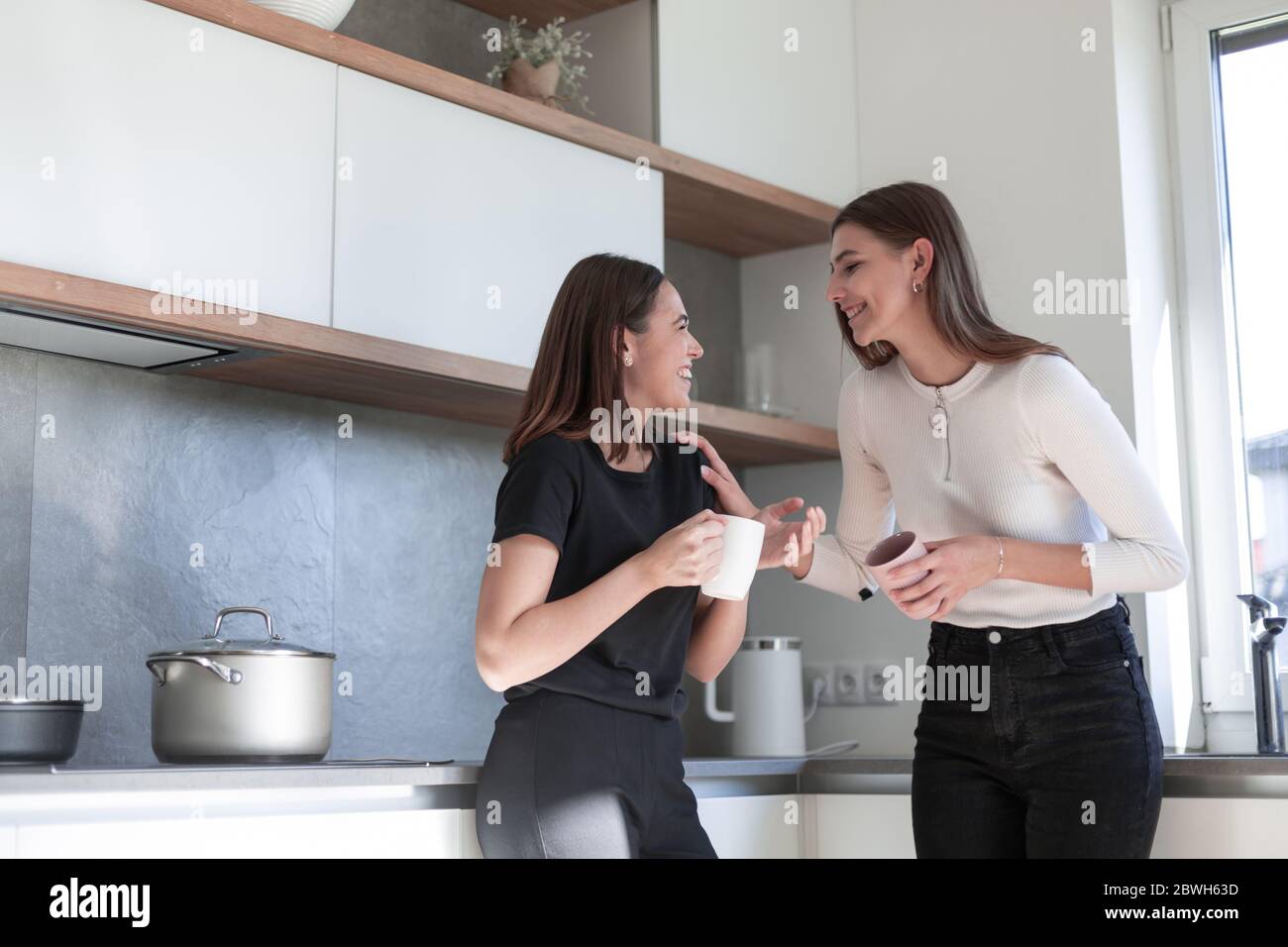 Zwei junge lachende Frauen stehen in der Küche und genießen Stockfoto