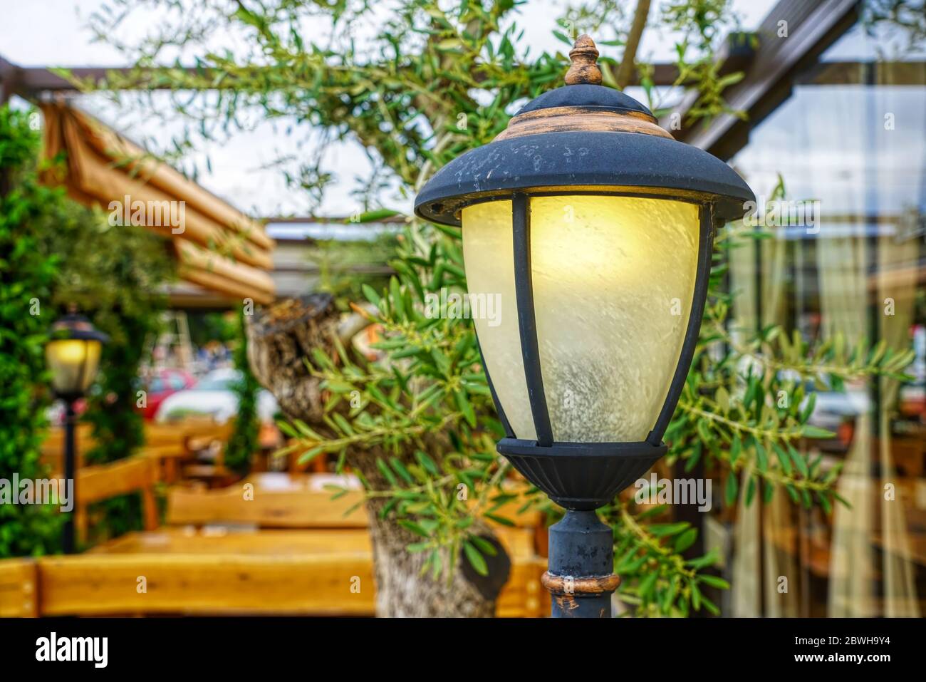 Gusseiserne Lampe in einem idyllischen Garten mit Holzbänken und Tischen Stockfoto