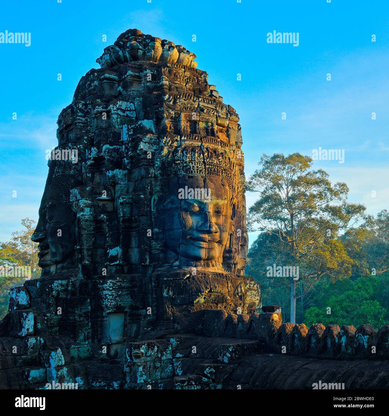 Ein Buddha-Gesicht beleuchtet bei Sonnenaufgang im Bayon-Tempel mit Regenwald im Hintergrund, Angkor Thom, Siem Reap, Kambodscha. Stockfoto
