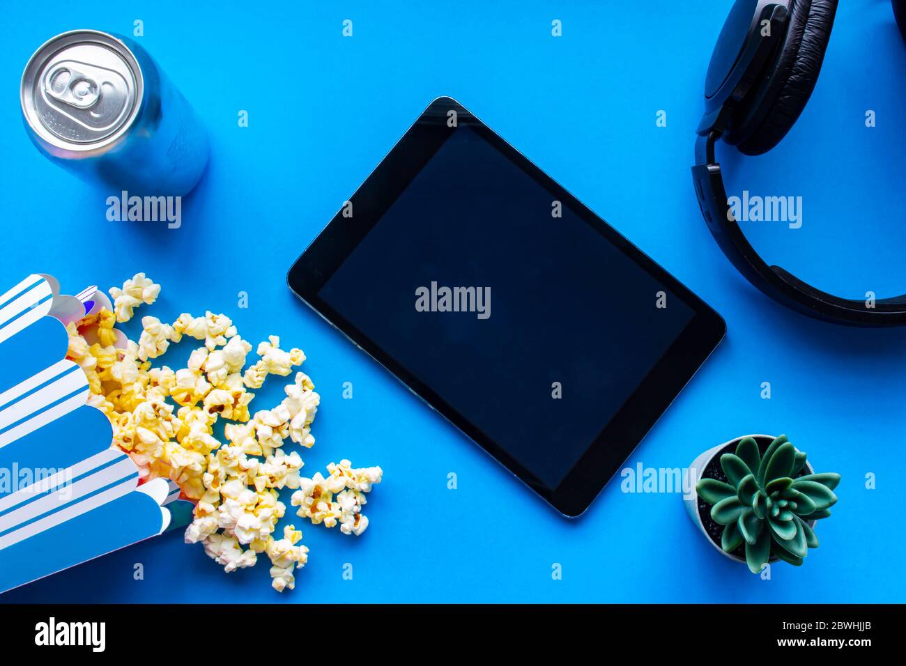 Ein Tablet auf blauem Hintergrund mit Popcorn und Kopfhörern Stockfoto