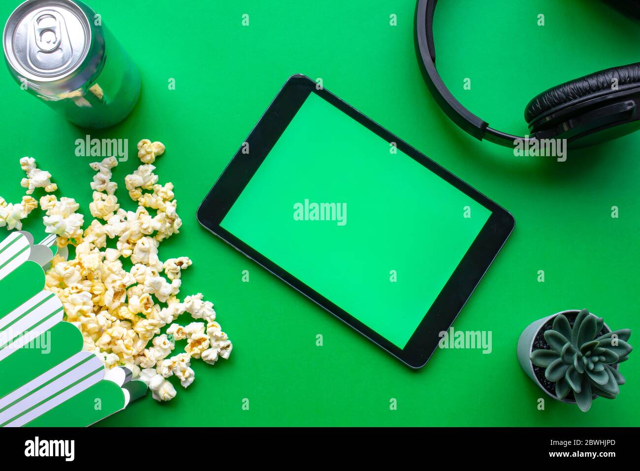 Ein Tablet auf grünem Hintergrund mit Popcorn und Kopfhörern Stockfoto