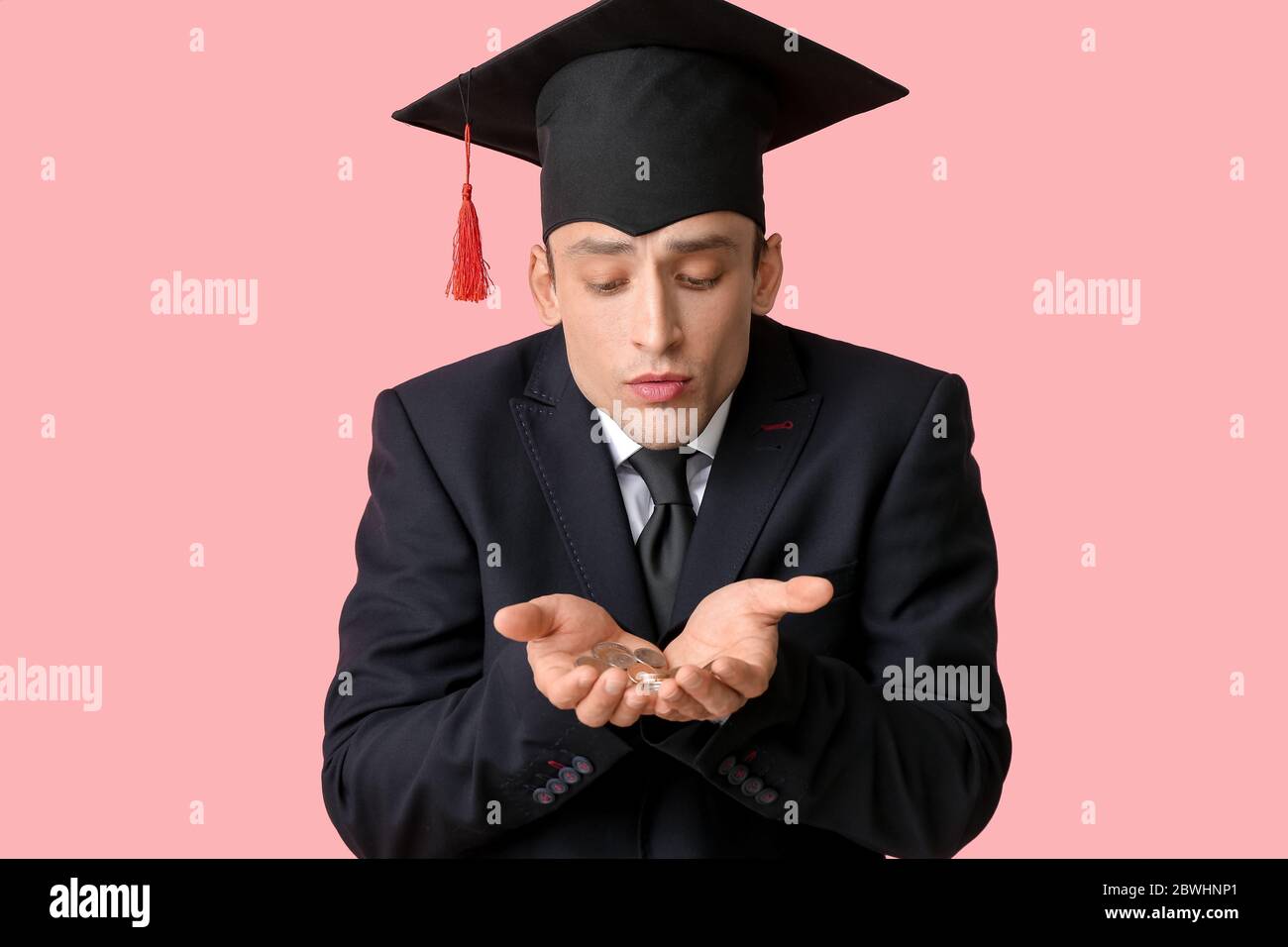 Junger Mann in Graduierung Hut und mit Münzen auf farbigem Hintergrund. Konzept der Studiengebühren Stockfoto