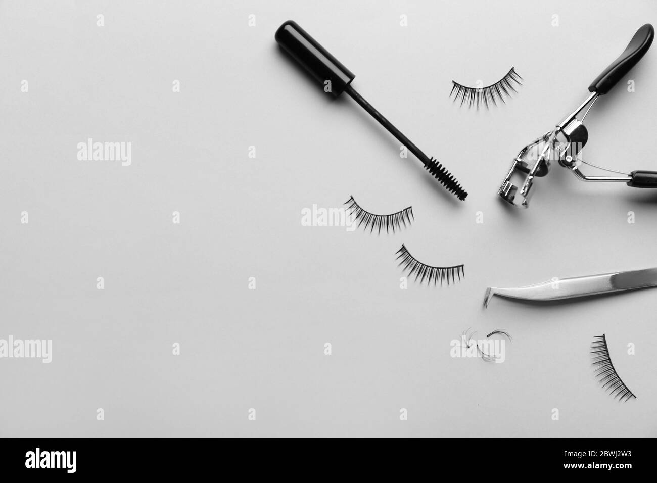 Mascara, gefälschte Wimpern, Pinzette und Lockenstab auf hellem Hintergrund Stockfoto