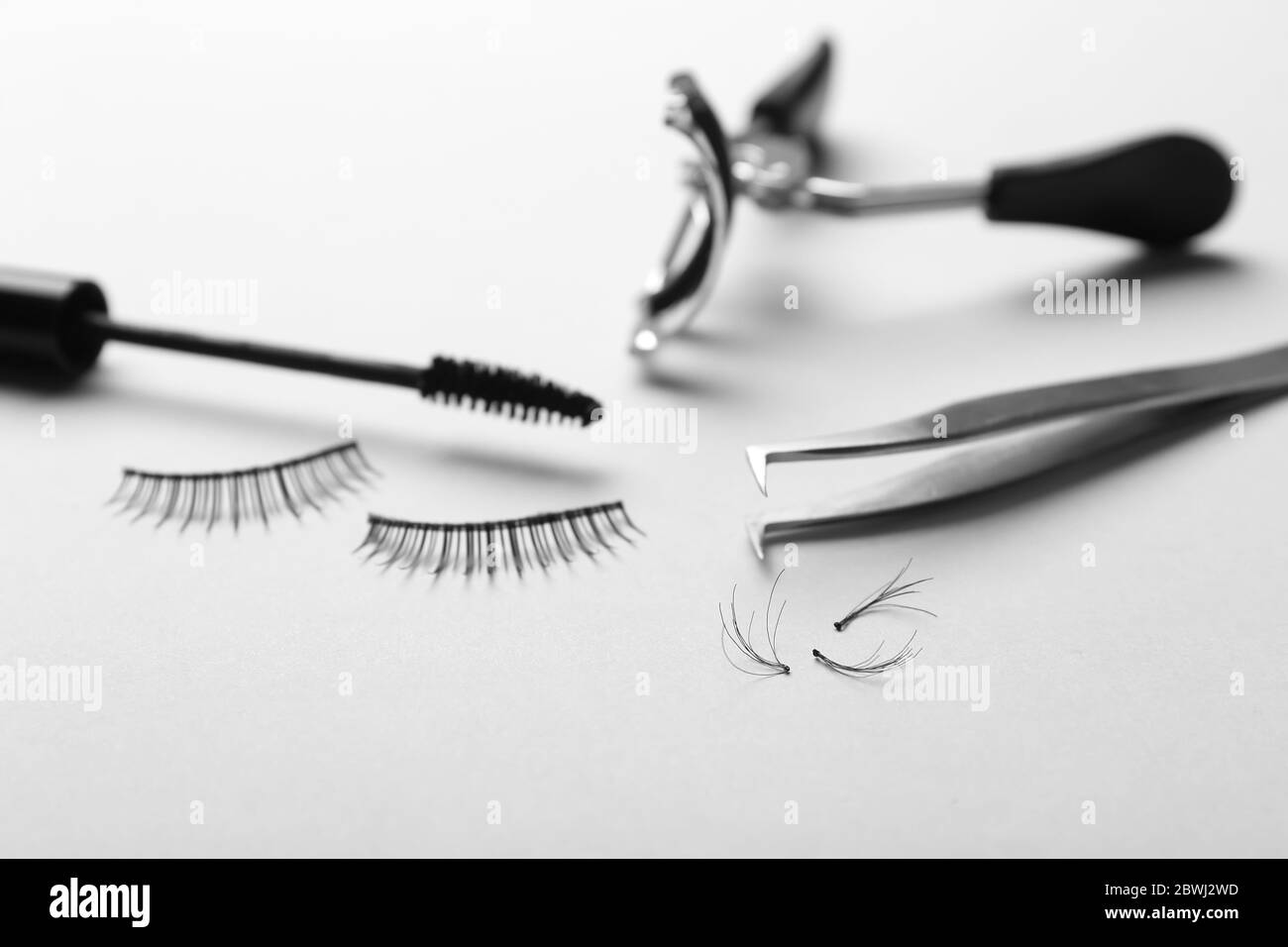 Mascara, gefälschte Wimpern, Pinzette und Lockenstab auf hellem Hintergrund Stockfoto