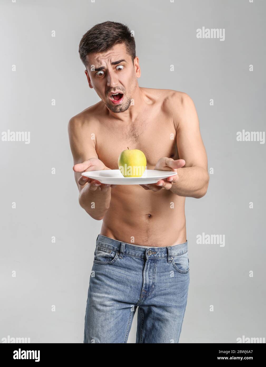 Erschrocken Mann mit Apfel auf grauem Hintergrund. Konzept der Magersucht Stockfoto