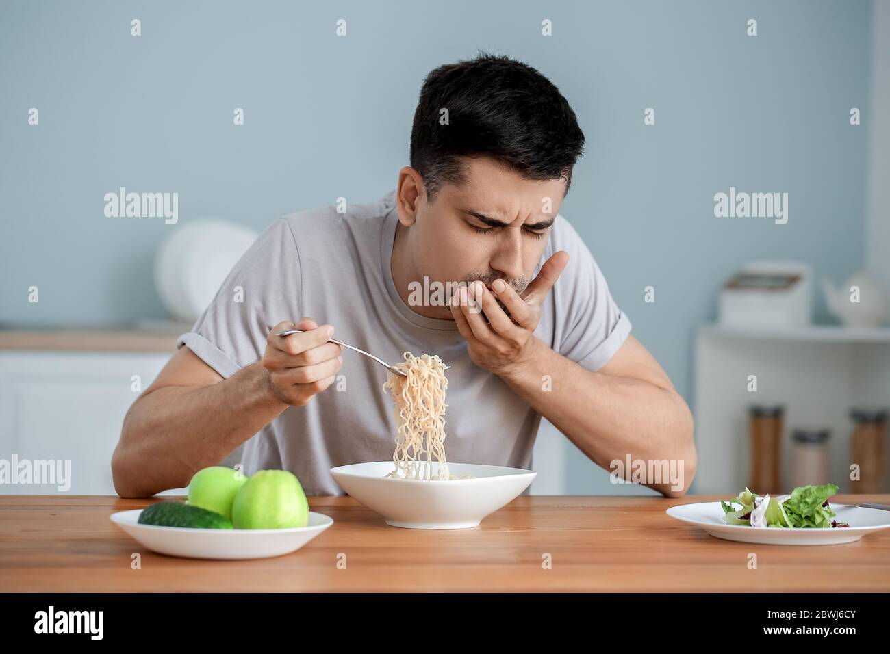Junger Mann mit Anorexie, der zu Hause Nudeln isst Stockfoto