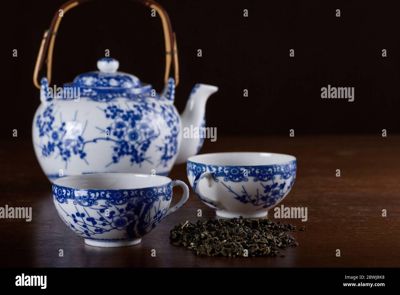 Alte chinesische Porzellan Teekanne mit zwei Tassen, mit grünem Tee auf dem Holztisch in Low Key Stockfoto