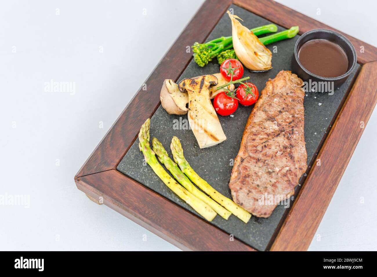 Gegrilltes Rindersteak Fleisch mit Gemüse auf Holzplatte. Luxus-Rindfleisch Steak auf weißem Hintergrund. Rindersteak bereit zum Servieren Stockfoto