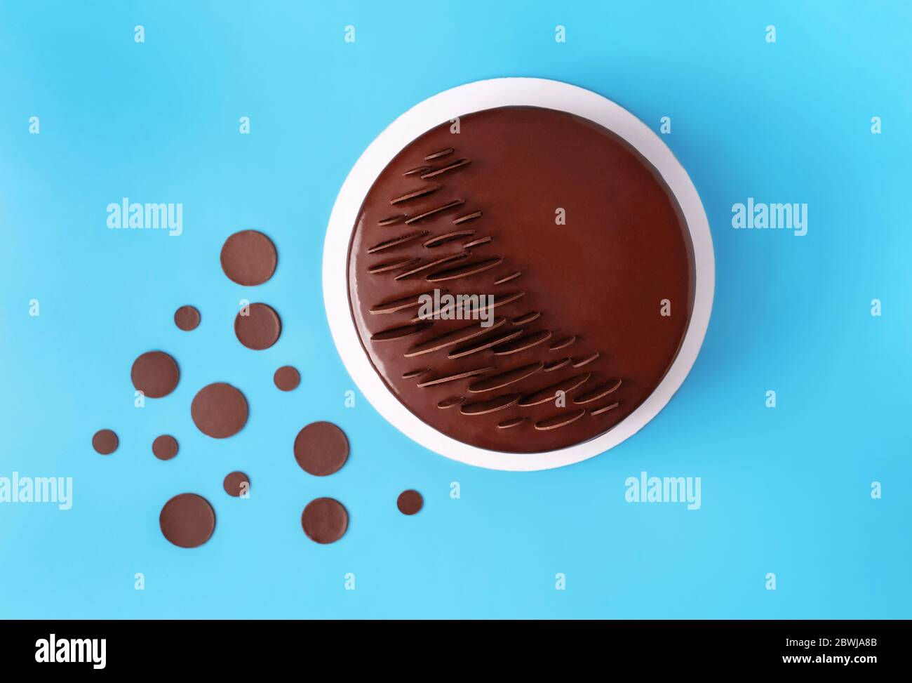 Dunkle Schokolade Mousse Kuchen mit Spiegelglasur bedeckt und mit runden Schokoladenstückchen auf blauem Hintergrund dekoriert. Moderner, stilvoller Kuchen. Flaches Lay-Design. Stockfoto