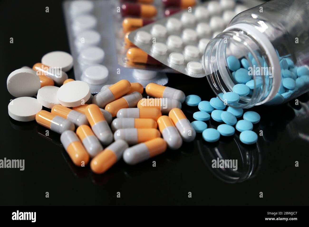 Pillen auf einem dunklen Glastisch, verschiedene Medikamente in Kapseln und Tabletten aus einer Flasche verstreut. Konzept der Apotheke, Antibiotika, Vitamine Stockfoto