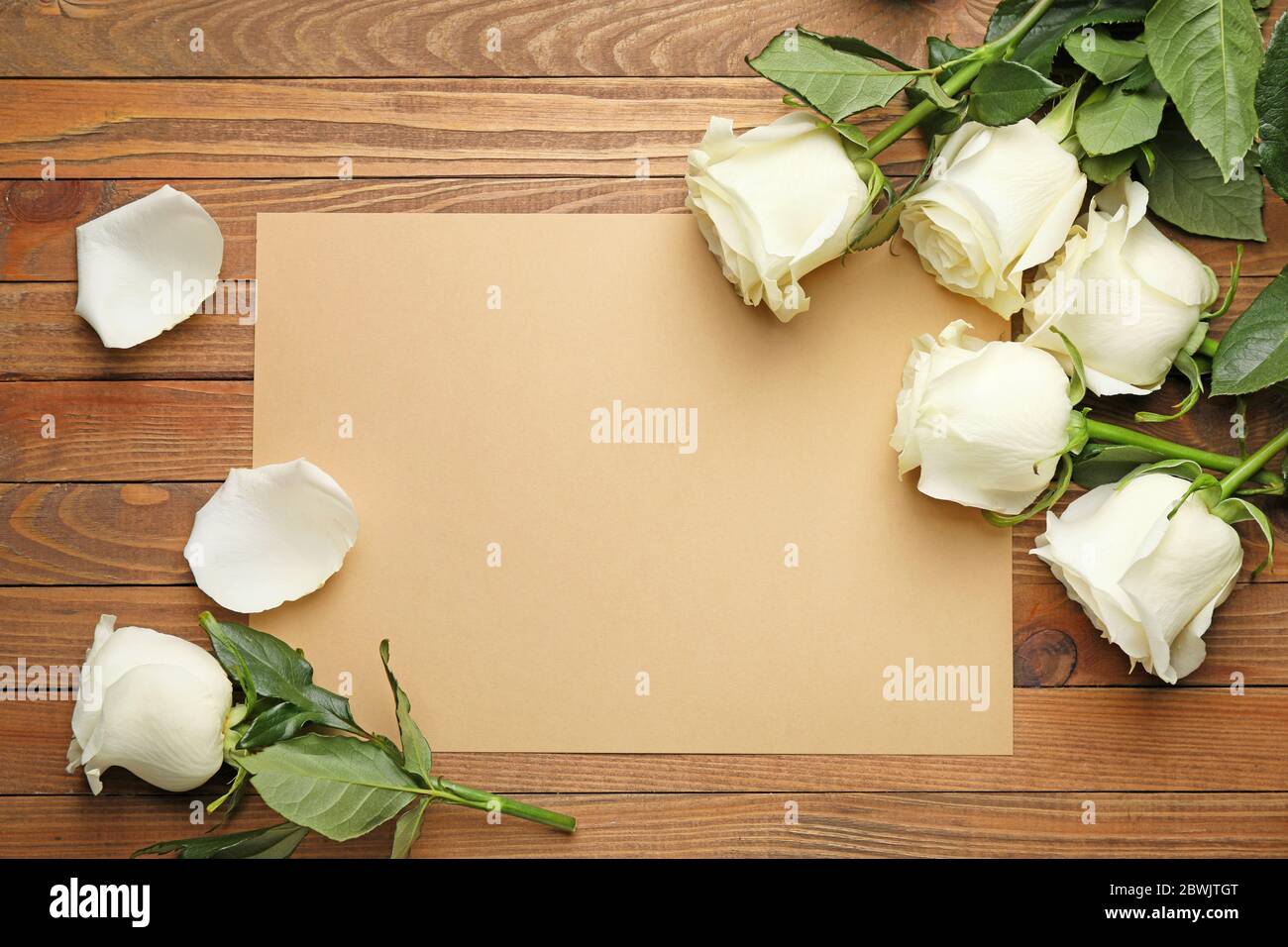 Schöne weiße Rosen und leere Karte auf Holzhintergrund Stockfoto