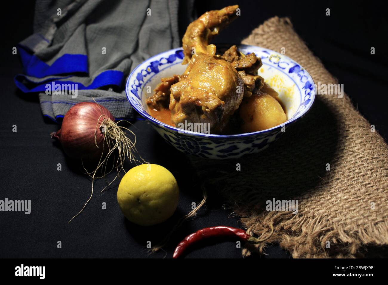 Gekochtes Hühnchen Curry in weißen Topf. Scharf und scharf Chicken Curry mit grüner Zitrone & Chili, Zwiebel isoliert auf schwarzem Hintergrund. Stockfoto