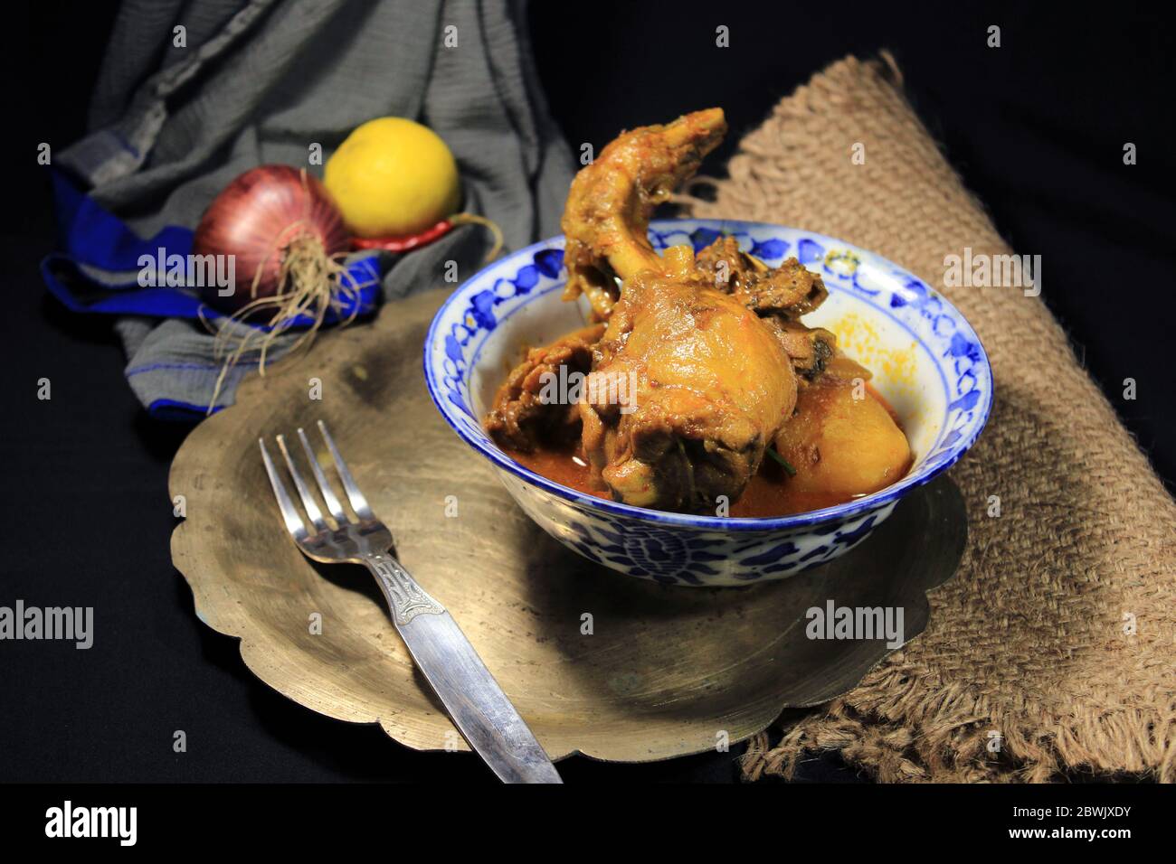 Gekochtes Hühnchen Curry in weißen Topf. Scharf und scharf Chicken Curry mit grüner Zitrone & Chili, Zwiebel isoliert auf schwarzem Hintergrund. Stockfoto