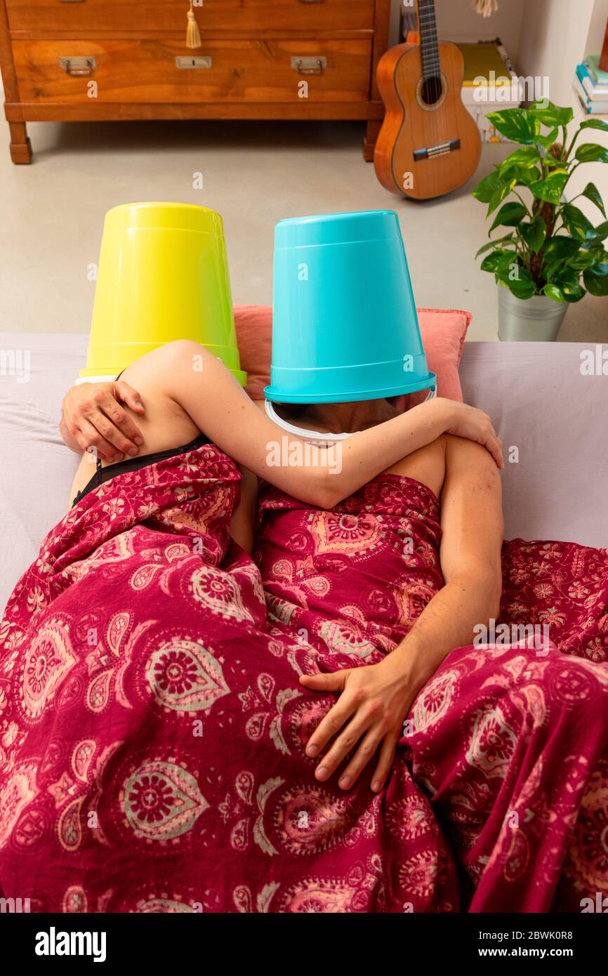 Junge Paare im Bett mit einem Eimer auf dem Kopf, sie machen Liebe oder Ruhe, aber sie sprechen nicht miteinander. Stockfoto