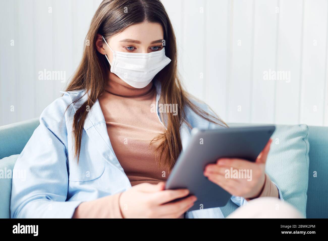 Kaukasische junge Frau in Maske verwenden Tablette auf dem Bett. Weiblich Online-Video während der Quarantäne ansehen. Student Studieren zu Hause. Stockfoto