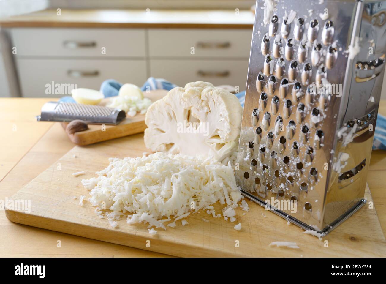 Reibe Blumenkohl mit einer Metallreibe als Reisersatz zum Kochen eine gesunde Low Carb oder ketogene Diät Mahlzeit auf einer hölzernen Küchenarbeitsplatte, selecte Stockfoto