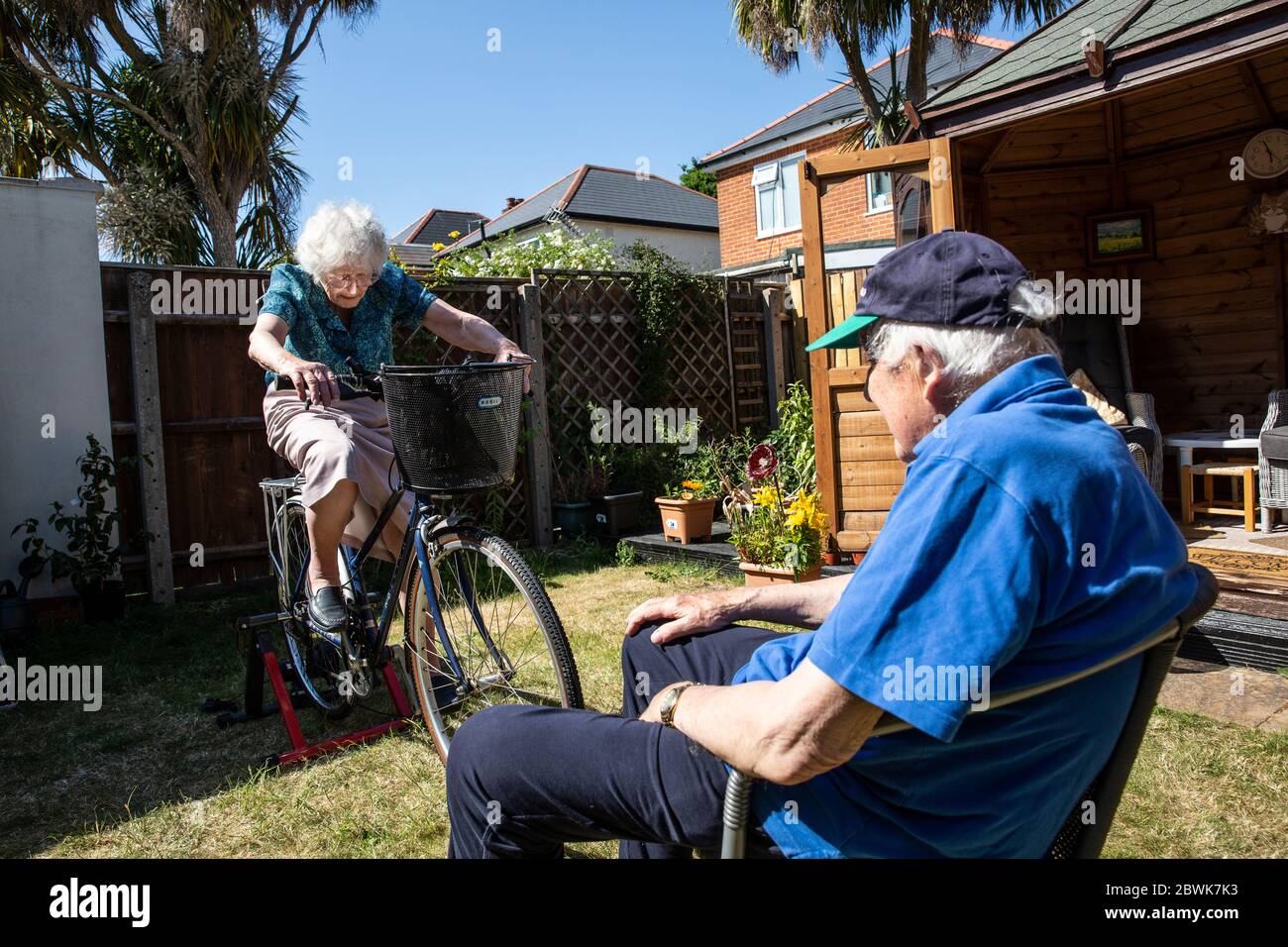 Ältere Paare beide in den 80ern halten sich fit auf einem Fahrradtrainer Stand in ihrem Garten während der Coronavirus Lockdown, Südwestengland, Großbritannien Stockfoto