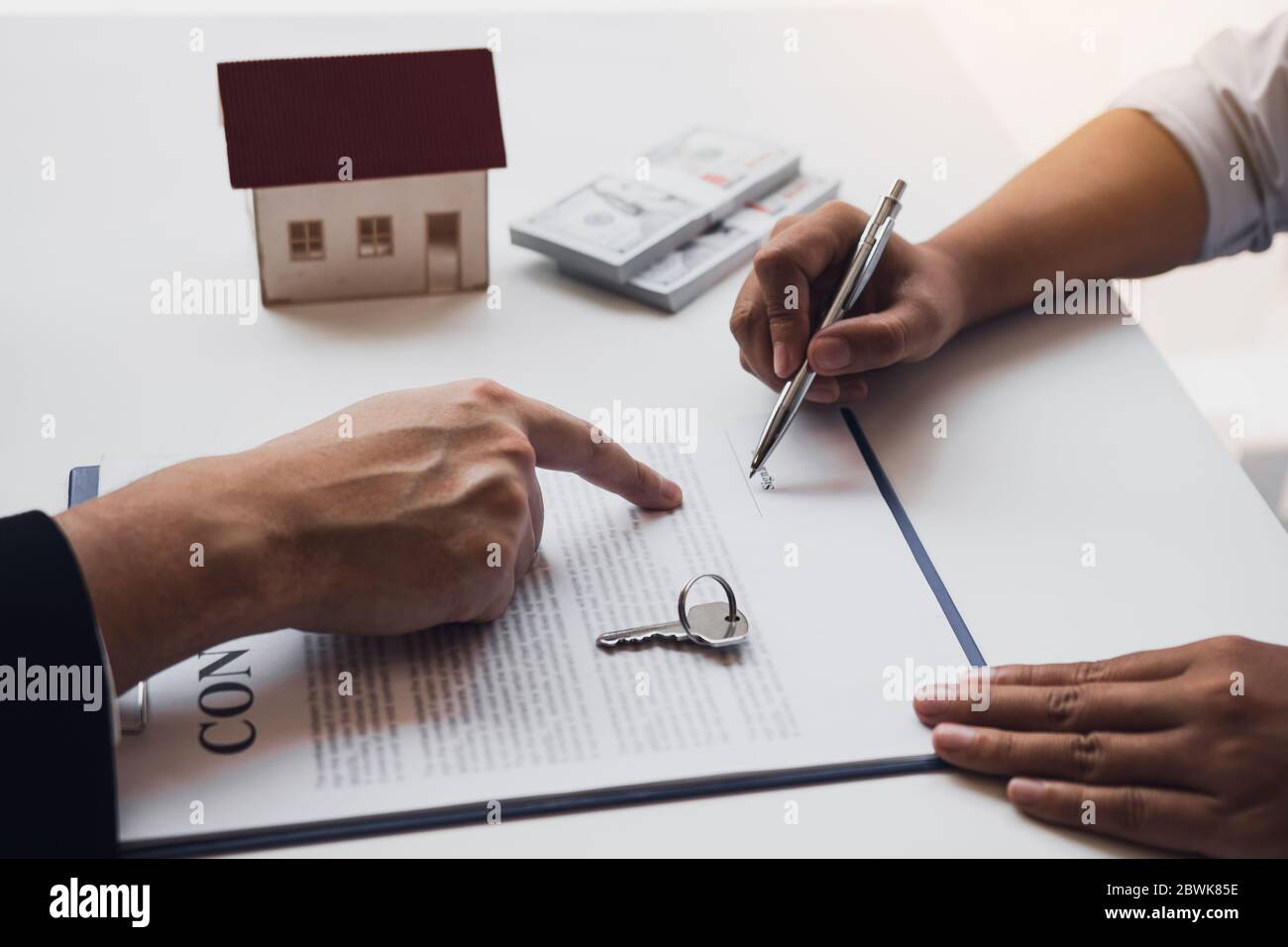 Neue Hauskäufer unterzeichnen einen Hauskaufvertrag am Schreibtisch des Agenten. Stockfoto
