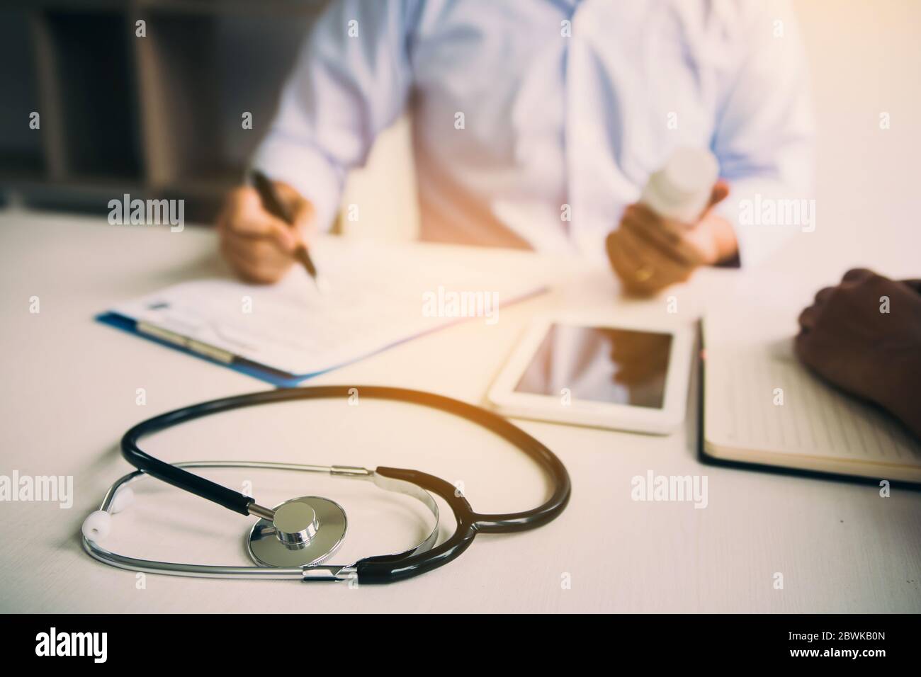 Selbstbewusster Arzt, der eine Pillenflasche hält und schreibt, während er mit einem älteren Patienten spricht und seine Medikamente im Büroraum überprüft. Stockfoto