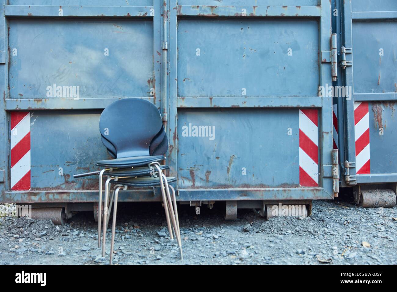 Alte Stühle stapeln sich als Sperrmüll vor Schutt-Containern auf Industriegelände Stockfoto