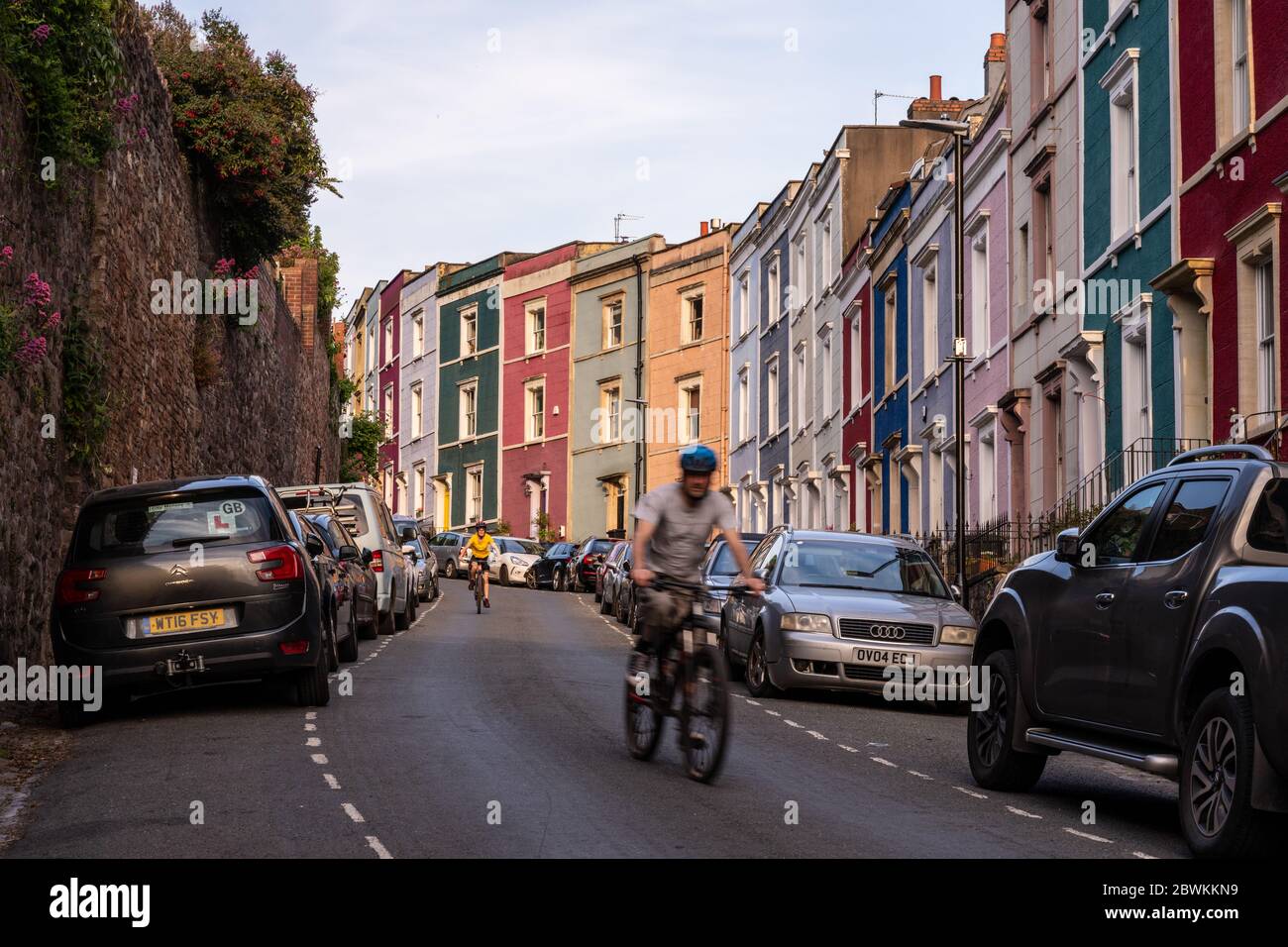 Bristol, England, Großbritannien - 9. Mai 2020: Zwei Radfahrer fahren an bunten Reihenhäusern auf einem steilen Hügel in Hotwells, Bristol vorbei. Stockfoto