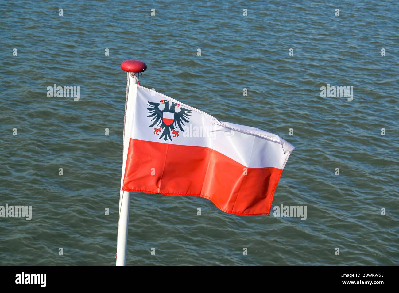 Flagge der Hansestadt Lübeck mit dem Doppeladler auf weißem und rotem Streifen flattert am Heck eines Bootes gegen das Wasser Stockfoto