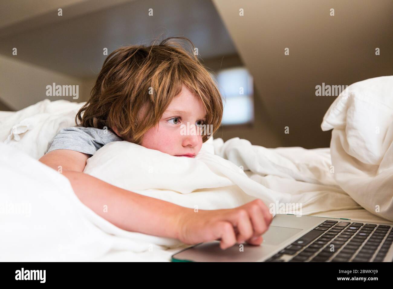6 Jahre alter Junge, der Laptop-Computer in seinem Schlafzimmer ansieht Stockfoto