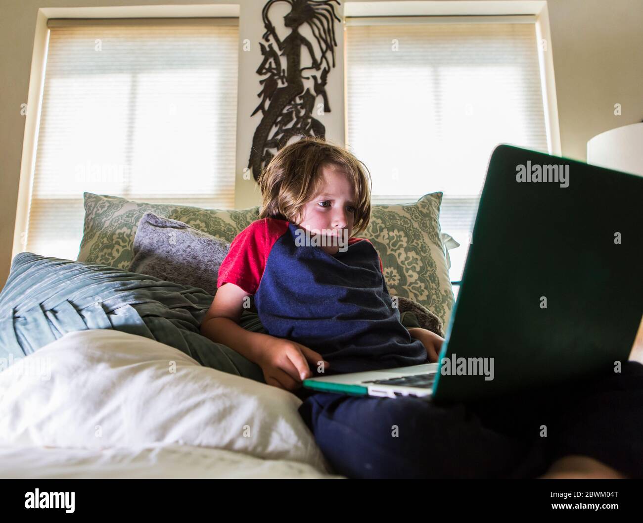 6 Jahre alter Junge, der im Bett liegt und Laptop anschaut Stockfoto