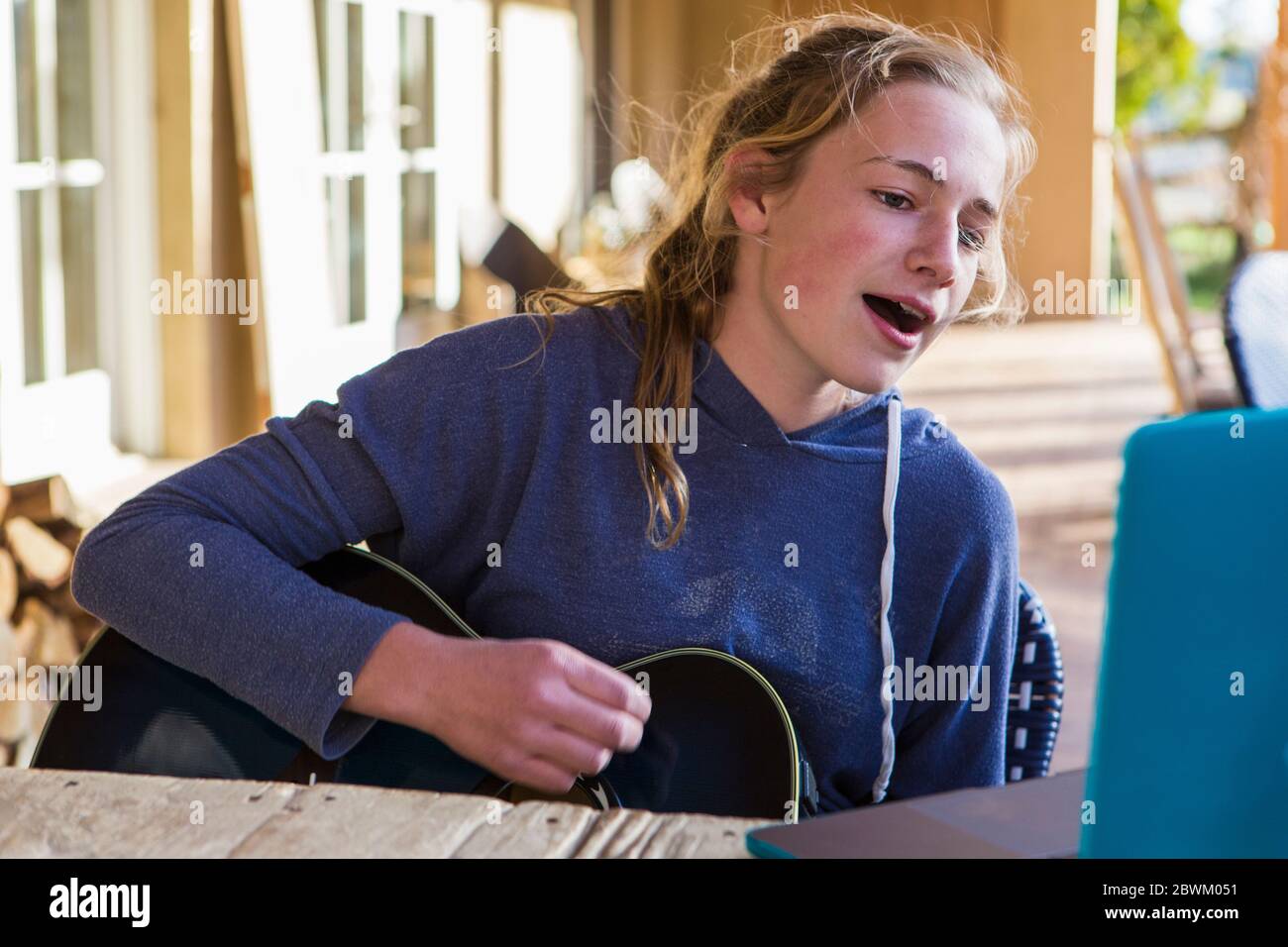 Ein Teenager-Mädchen, das Laptop anschaut, singt und Gitarre spielt Stockfoto