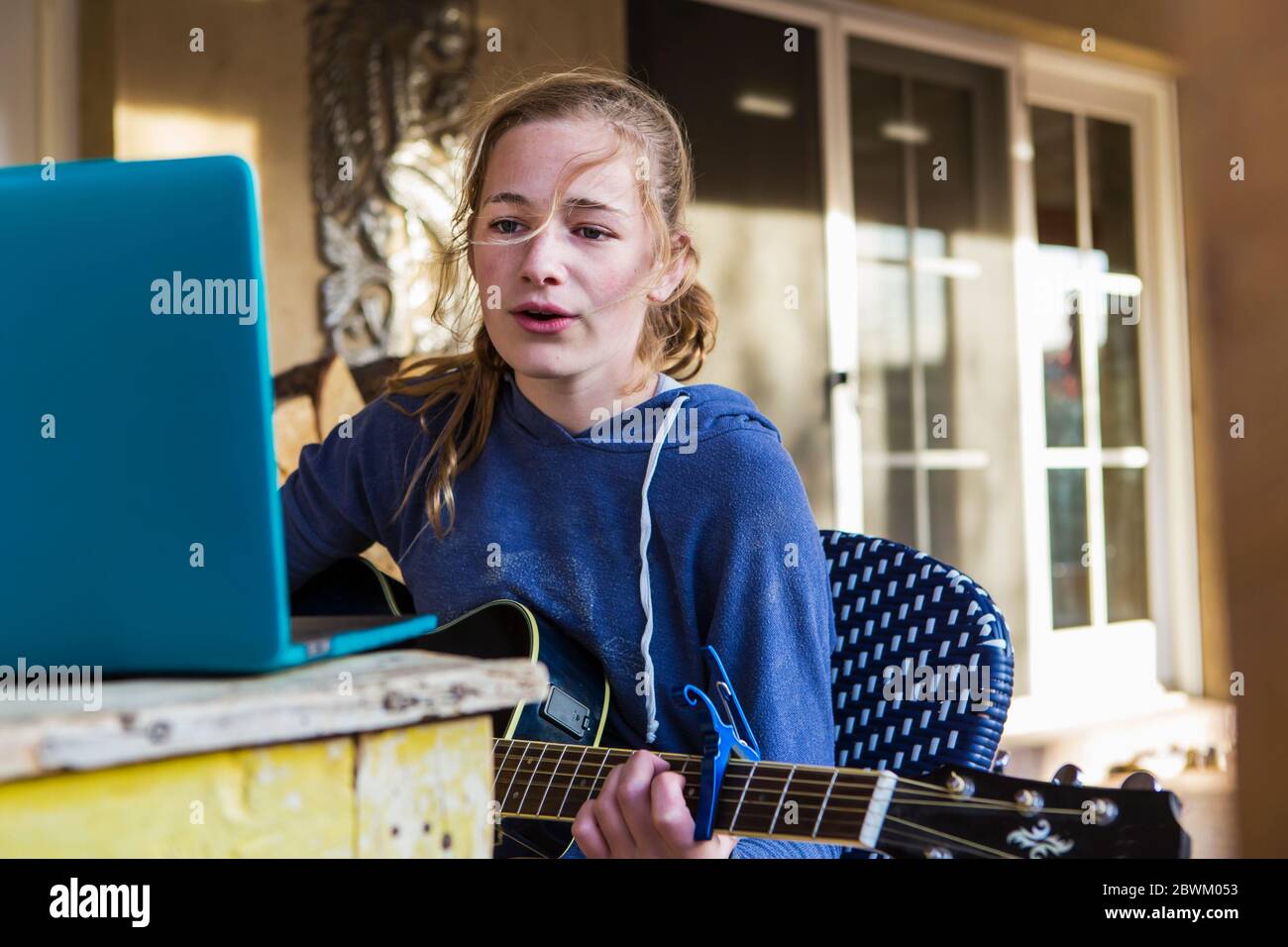 Ein Teenager-Mädchen, das Laptop anschaut, singt und Gitarre spielt Stockfoto