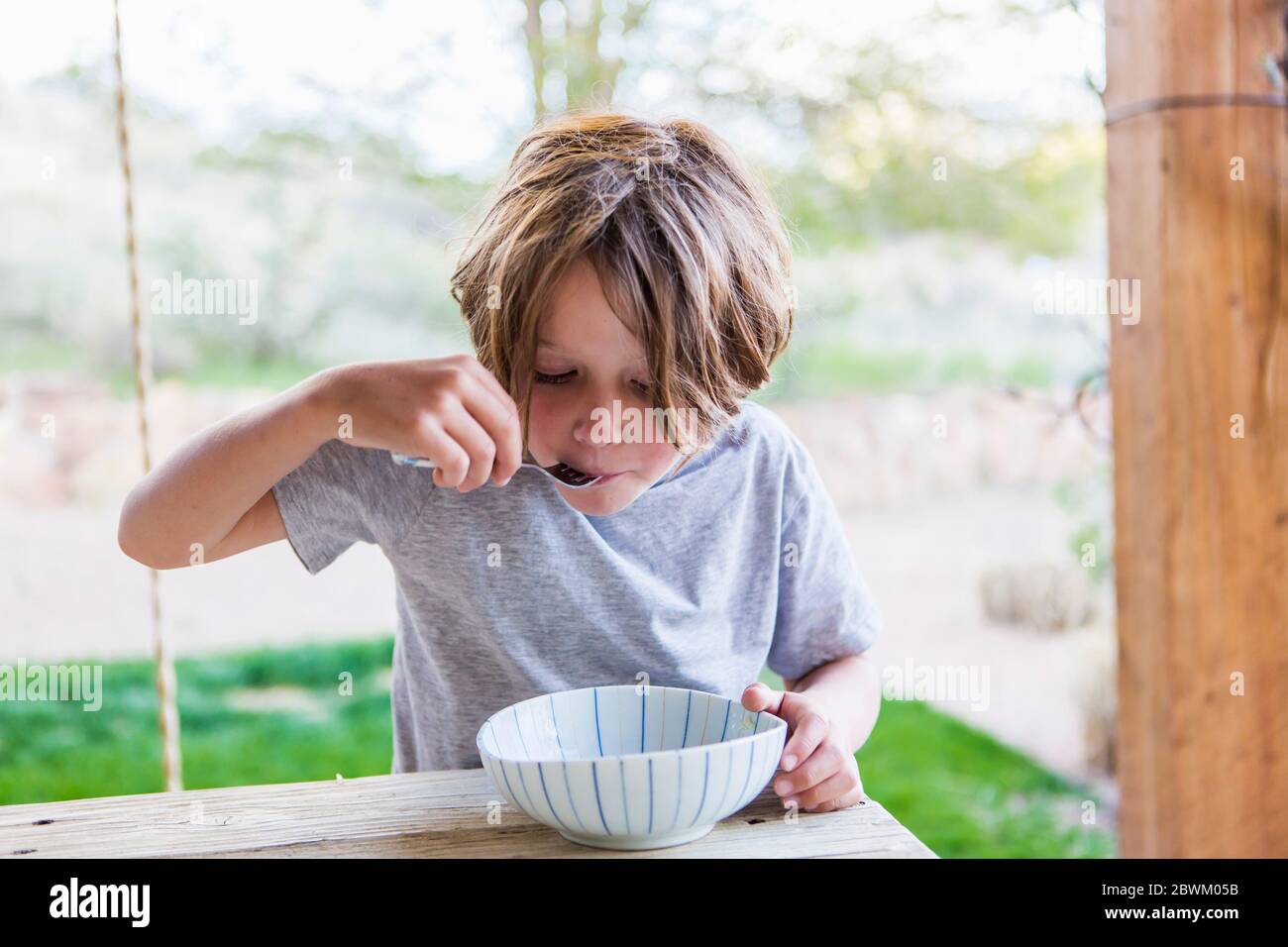6 Jahre alter Junge, der Reis auf seiner Terrasse isst Stockfoto