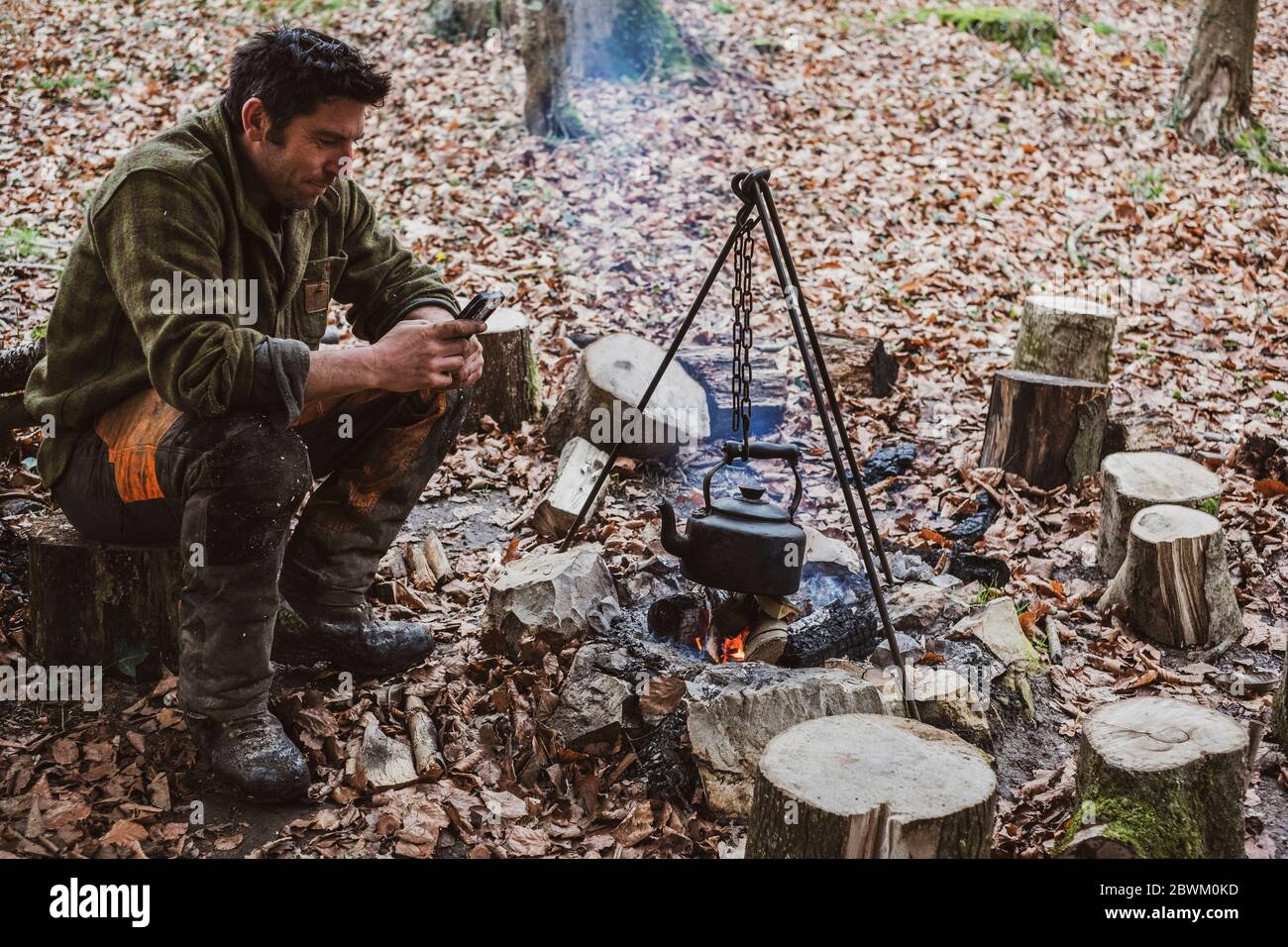 Mann sitzt am Lagerfeuer in einem Wald, kochender Wasserkessel. Stockfoto